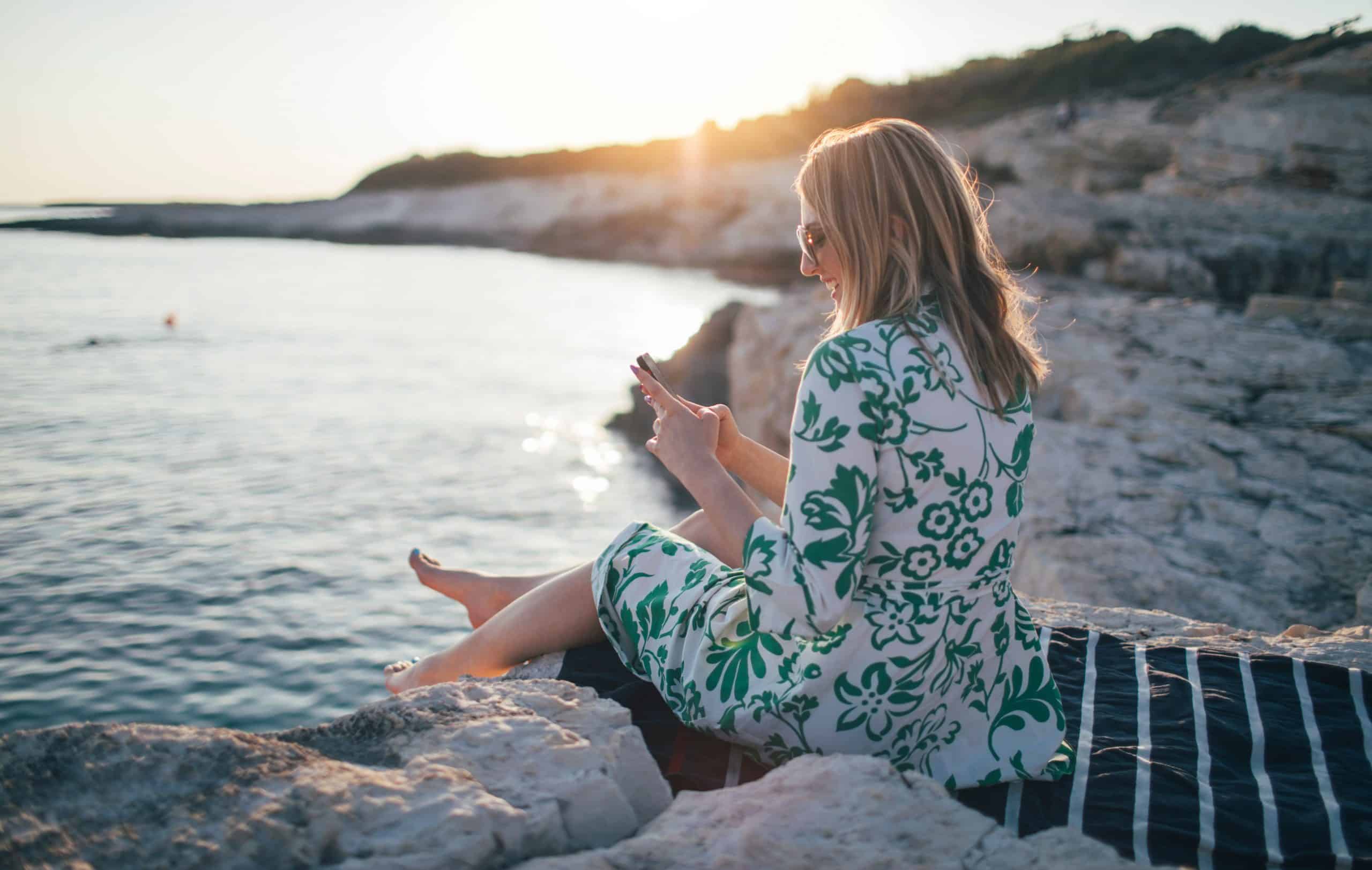 A woman sitting on the water, implementing an AI travel planner to enhance her vacation itinerary.