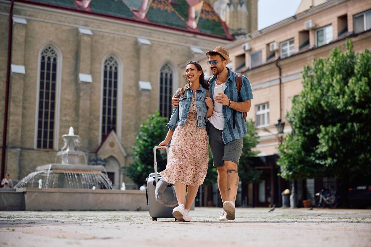 A couple strolling through a picturesque city square with luggage in tow, enjoying the perks of personalized travel rewards that make each destination feel special.