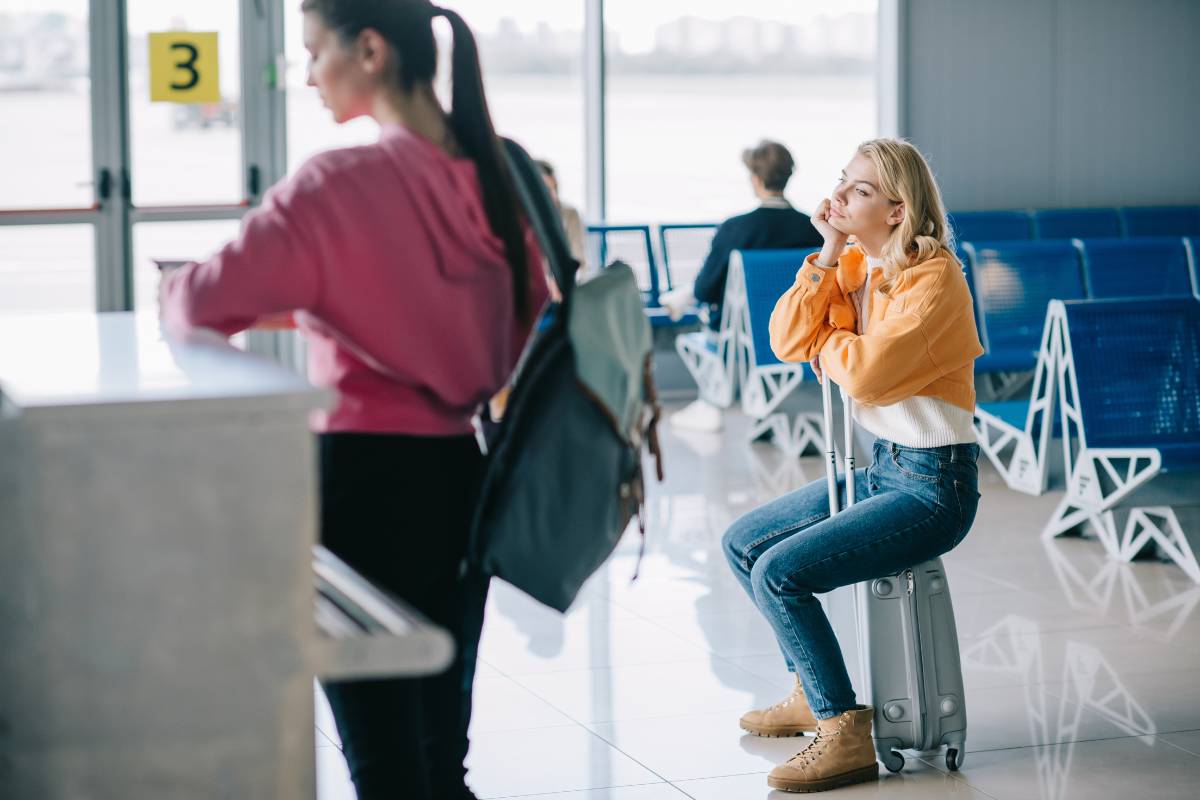 Young woman sitting on a suitcase in an airport terminal, appearing bored, illustrating strategies on how to reengage customers