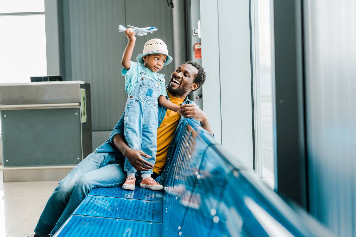 Smiling father and young child playing with a toy airplane while sitting on airport seating, symbolizing connection and joy, ideal for referral loyalty programs.