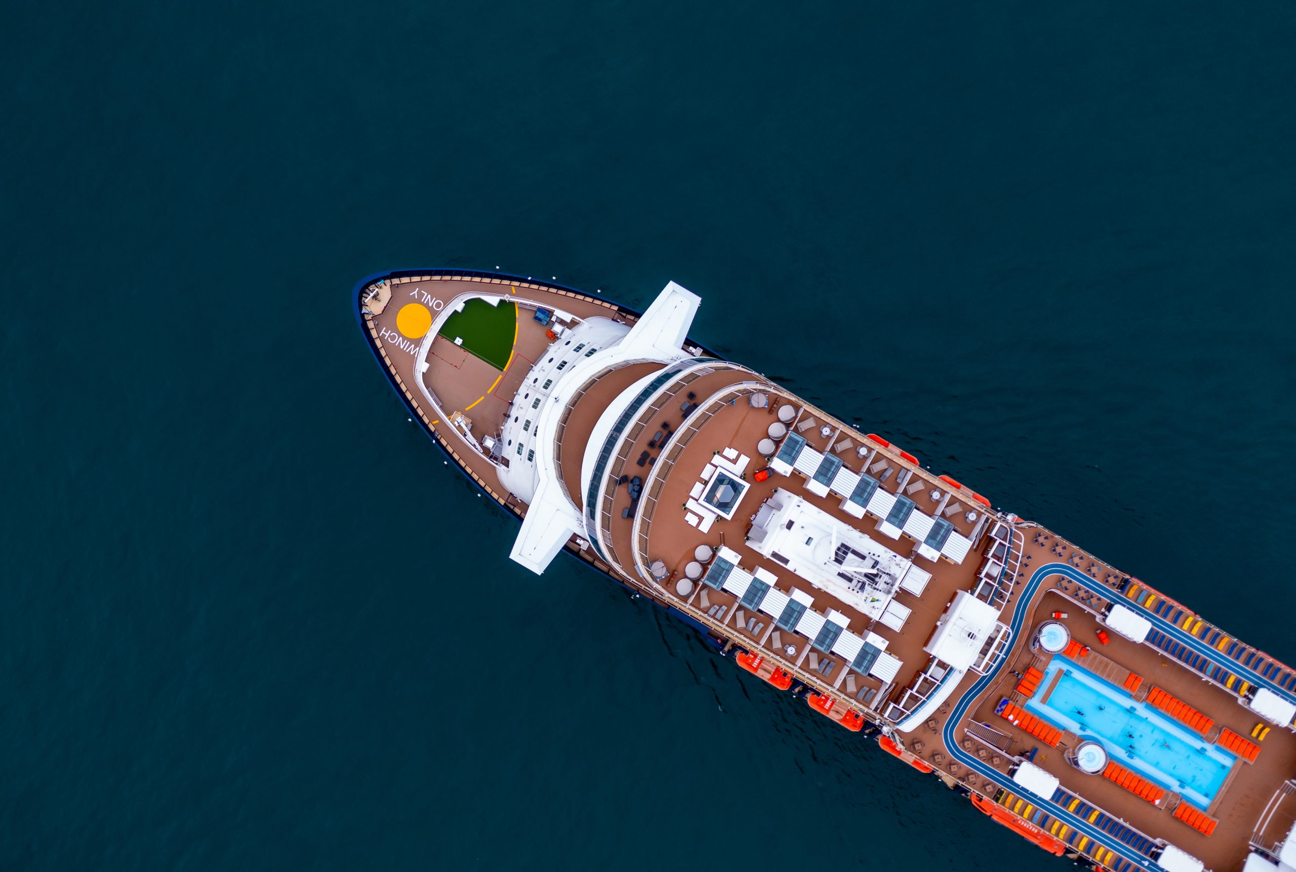 Aerial view of a cruise ship decked out with pools and leisure areas, showcasing the full experience of cruise benefits as it glides across the open ocean.