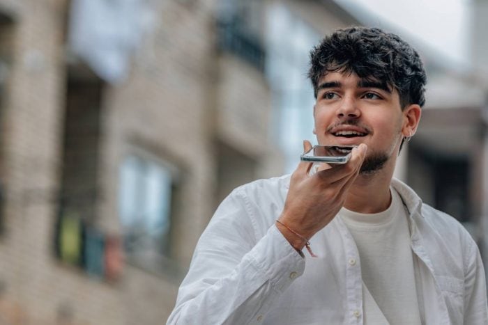 A young man speaks into his phone, demonstrating the convenience of voice booking AI for seamless travel planning.