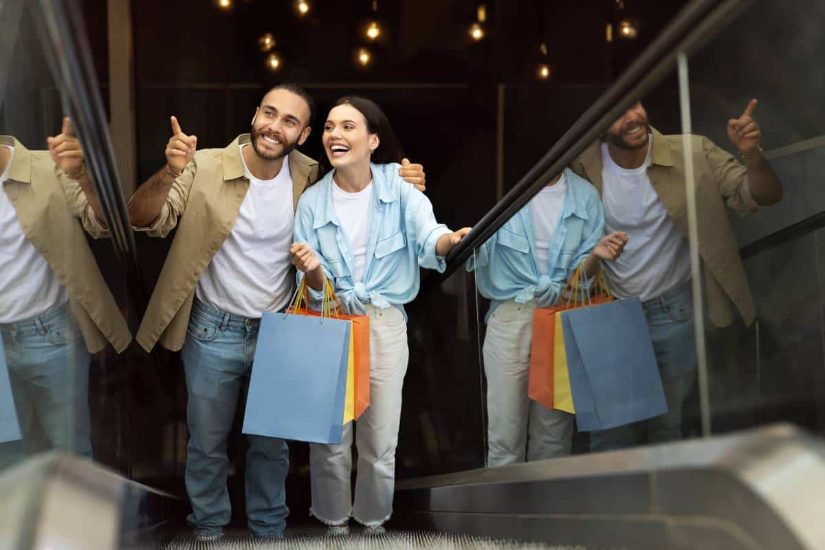 Two shoppers enjoying their purchases on an escalator, representing loyalty travel rewards for retail customers